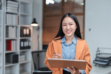Young professional woman working diligently on a project, jotting down notes on her clipboard while smiling in a bright, modern office filled with natural light and stylish decor