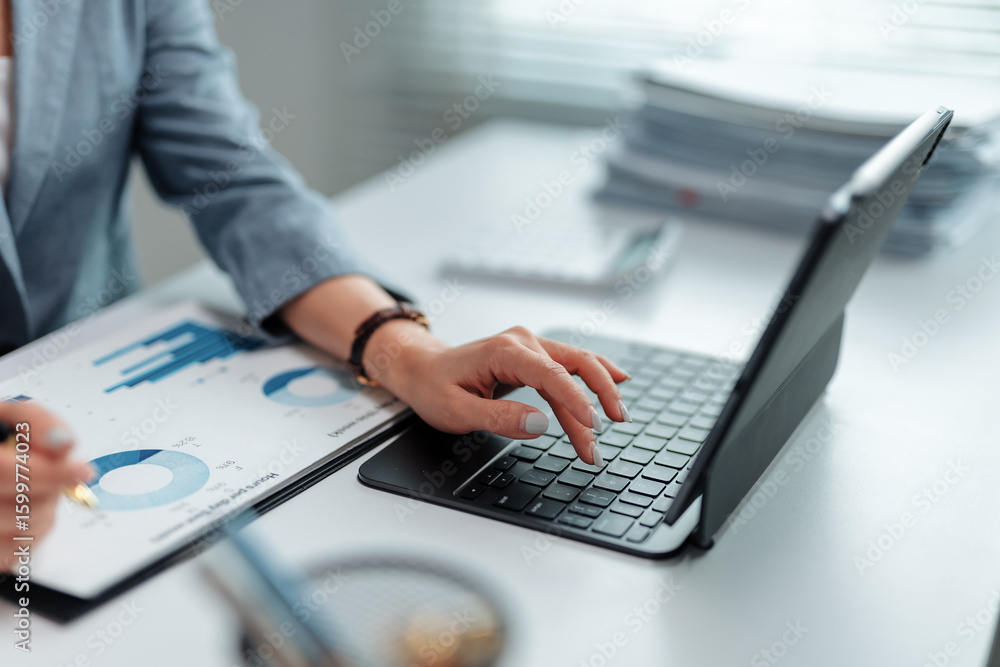 Poster businesswoman is holding a pen and analyzing financial charts while typing on a tablet keyboard in a
