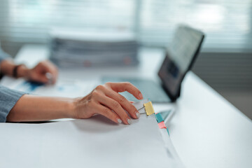 Office worker attaching documents with a paper clip while focused on tasks at a modern, tidy desk....