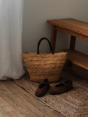 A straw basket bag, brown suede shoes on a jute carpet near a bench in the hallway