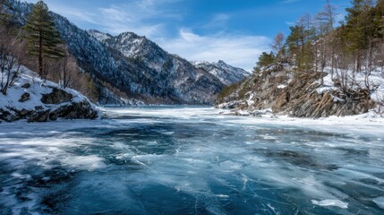 Beautiful winter scene showcases a frozen river winding through snow-covered mountains. Pine trees dot the landscape under a bright blue sky, creating a tranquil natural setting.