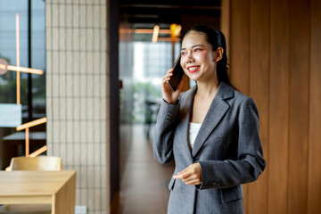 Young manager wearing suit using smartphone, smiling and walking in the hallway of a modern office building, having a pleasant conversation