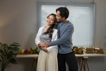 Happy asian couple embracing in their kitchen with fresh fruits and takeaway boxes on the table in the background, enjoying their time together