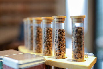 Glass tubes with wooden lids holding coffee beans of various roasting levels, arranged on a wooden...