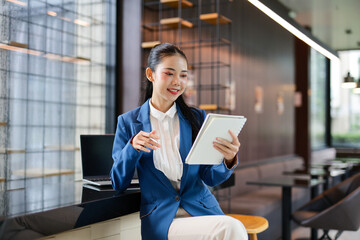 Young asian businesswoman using tablet and working on laptop while sitting in modern office lobby,...