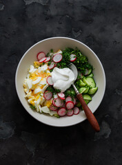 Eggs, cucumbers, radishes, green onions and Greek yogurt salad on a dark background, top view