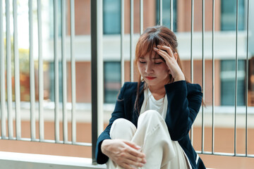 Young asian businesswoman is sitting on the balcony of an office building, suffering from a bad...