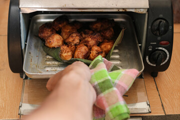 one hand takes a portion of crispy fried bananas in a baking tray lined with banana leaves that are heated in the microwave, the photo was taken from a high angle at close range