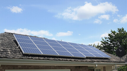 Fototapeta premium Residential rooftop solar panel array under a partly cloudy sky, mounted on grey shingles, near greenery and a satellite dish