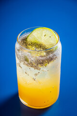 A vibrant drink mixes citrus and chia seeds, served in a glass on a bold blue surface