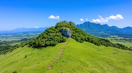 Naklejka premium Aerial View of Lush Green Hill and Distant Mountains Under a Blue Sky