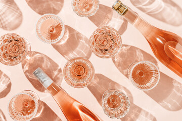 Minimal pattern from wine bottle and glasses of rose wine or champagne on pink with shadows and...