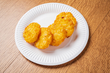Savory potato treats sit on a disposable plate, showcasing a delightful hue and texture