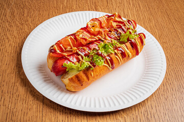 A hot dog with lettuce, ketchup, and mustard sits on a paper plate at a casual gathering
