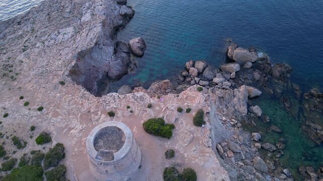 Carefree woman in pink dress in Yoga tree pose enjoying freedom and breathtaking view on Ibiza island near Torre des Savinar at sunset. Smooth aerial view flight speed ramp hyper motion time lapse