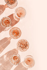 Minimal summer party concept, set glasses of rose wine or champagne on pink with shadows and light...