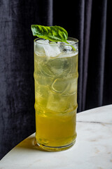 A vibrant green cocktail filled with ice and fresh basil sits elegantly on a marble surface