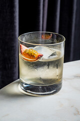 A beautifully crafted cocktail with ice, featuring a slice of fruit, positioned on a marble table