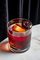A cocktail with ice and a cherry garnish sits on a marble table