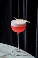 A refreshing pink cocktail sits elegantly on a marble surface, adorned with a delicate leaf garnish