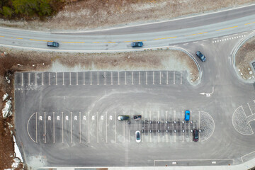 Electric vehicle approaches charging station within parking lot. Grey asphalt with numerous parking lines suggests quiet moment at modern facility