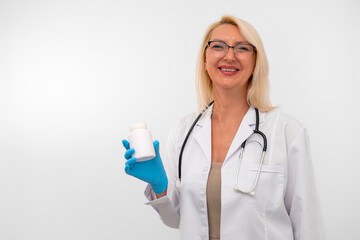 Confident female medical professional in lab coat and gloves showing a jar of vitamins. Studio shot, white background with copy space 