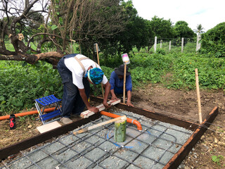 Construction workers are pouring a concrete mixture onto the slab of a septic tank.