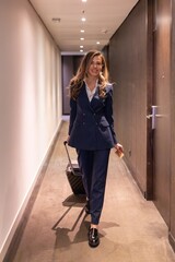A poised businesswoman in a tailored navy suit strides through a modern corridor with stylish...