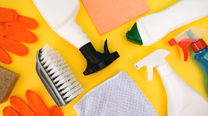 Cleaning bottles, rag, sponge, brush and orange rubber gloves on yellow background