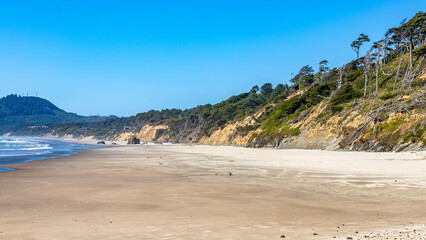 A serene sandy shoreline meets gentle ocean waves, backed by green forested hills under a clear blue sky. Perfect for themes of relaxation, coastal travel, and the natural beauty of the seashore.