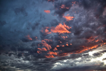 A dramatic and moody sky filled with dark, stormy clouds illuminated by vibrant orange and pink sunset light.
