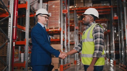Side view of Caucasian handsome middle-aged male boss wearing hard hat standing in big warehouse...