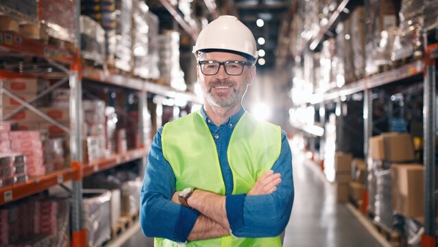Handsome Caucasian man using tablet browsing online while walking in warehouse of modern factory. Middle-aged male manager doing inventory in storehouse holding digital device and looking at screen