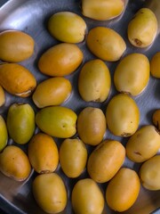 Fresh ripe dates (Phoenix dactylifera) arranged in a stainless steel plate, showcasing shades of yellow and orange.