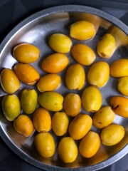 Fresh ripe dates (Phoenix dactylifera) arranged in a stainless steel plate, showcasing shades of yellow and orange.
