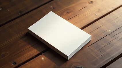 A blank, rectangular book or box rests on a dark brown wooden surface, illuminated by soft, warm light.  The wood grain is visible, and the object's smooth, white surface contrasts sharply