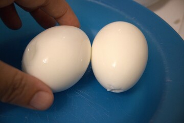 Two boiled eggs on blue plate close up with hand.