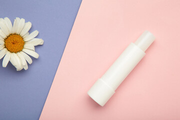 Lip balms and chamomile flowers on pink background.