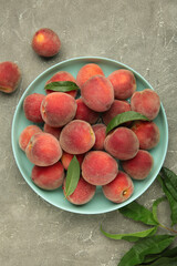 Sweet peaches and leaves on mint plate on grey concrete background. Vertical photo