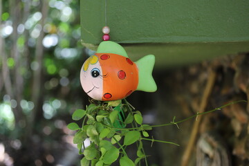 Colorful fish-shaped hanging planter with a smiling face, holding trailing green vines. A whimsical...
