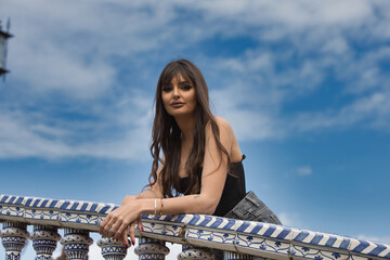 pretty young brunette woman looks out from the tiled railing of a bridge in the square of spain in...