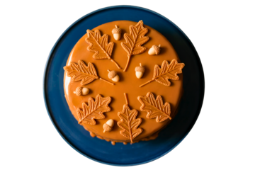 Top view of a fall-themed Halloween cake topped with caramel leaves and tiny candy acorns, placed on a blue ceramic plate