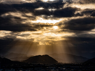 流れる雲の間から山の向こうに太陽の光が差す