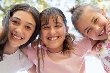 Happy children or teenage girls embracing each other, hanging out, having fun, and smiling at the camera against a sky background, a group of joyful kids playing together outside