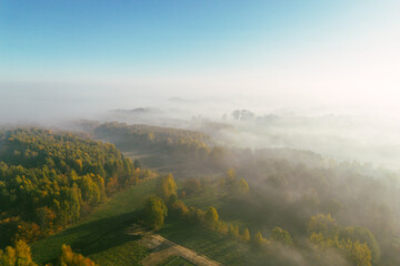 Naklejka premium Fog rolls over autumn trees and fields at sunrise