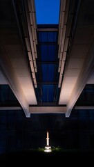 Obraz premium Modern Architecture at Night: Illuminated Sculpture Between Concrete Buildings, Serene Blue Hour Mood.