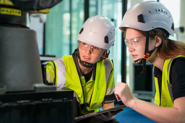 Two people wearing safety gear and looking at a piece of equipment. Concept of Industry 4.0 with diverse engineers collaborating on automation technology.