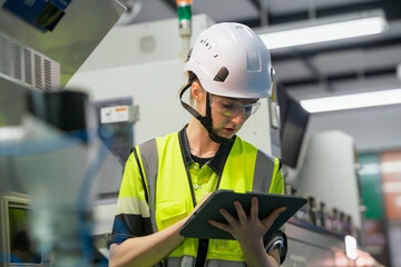 A worker wearing a yellow and black vest is looking at a tablet. Concept of Industry 4.0 with...