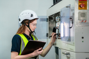 A woman wearing a yellow vest and a white helmet is writing on a clipboard. Concept of Industry 4.0...