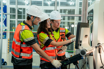 Three people wearing safety gear are working on a computer. Concept of Industry 4.0 with diverse...